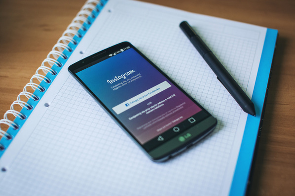 Photograph of a spiral, notebook, pen, and smart phone on the Instagram login page.