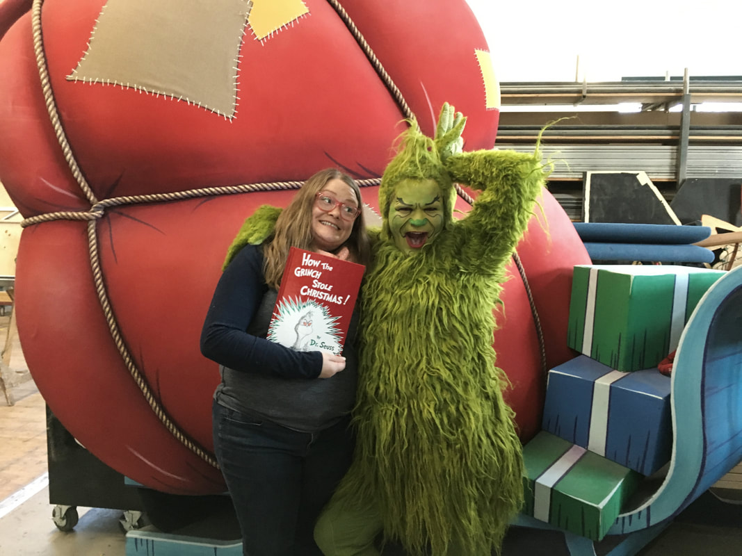 Pictured: Kendra and the Grinch pose in the CTC scene shop and a set piece that looks like a sleigh filled with a big Santa bag.